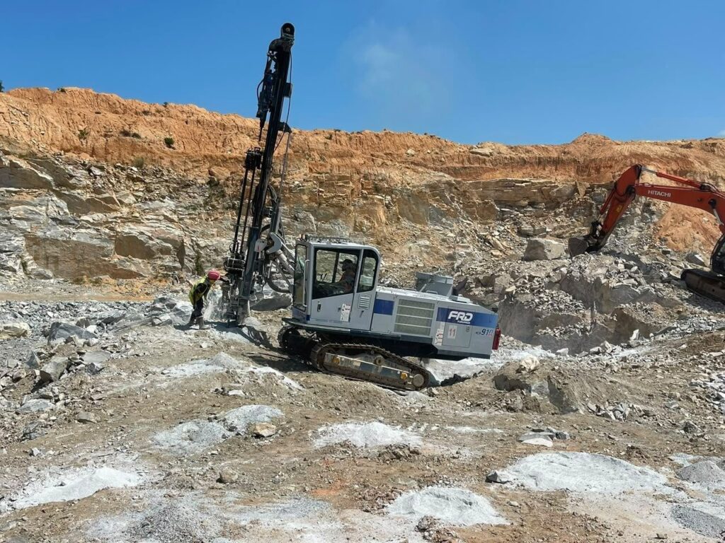 Drill rig and excavator carrying out rock breaking for mine haul road construction